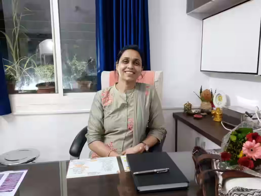 Dr. Shraddha Bihani smiling at her desk in a well-lit office with blue curtains and floral decor.